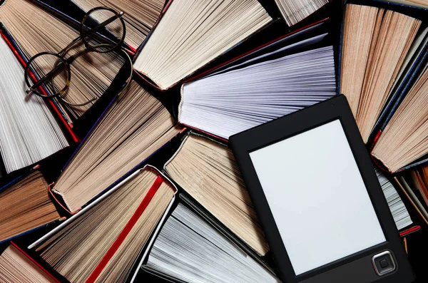 The e-book with a white screen lies on the open multi-colored books that lie on a dark background, close-up Stock Image