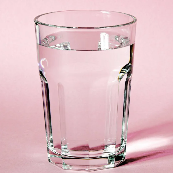 Wasserglas mit starken Schatten auf rosa Hintergrund — Stockfoto