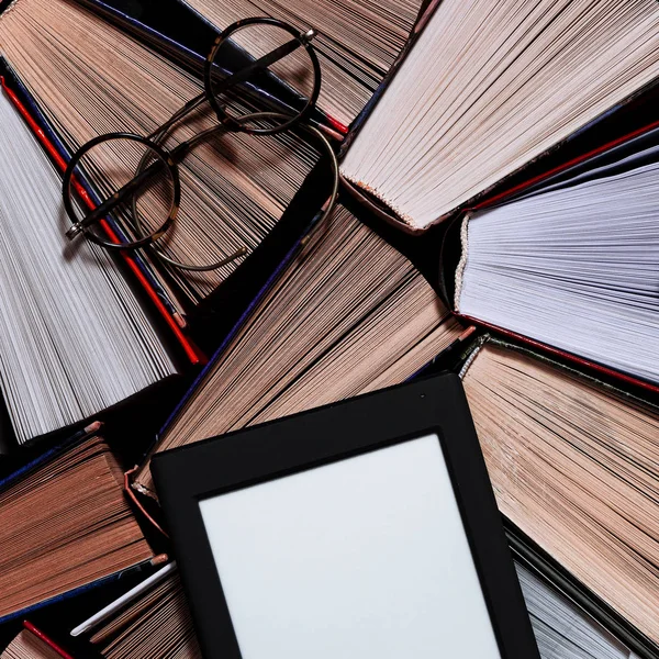 The e-book with a white screen lies on the open multi-colored books that lie on a dark background, close-up — Stock Photo, Image