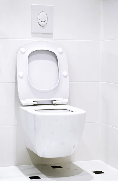 Interior. Um vaso sanitário branco pendura em uma parede de azulejo branco em um banheiro branco — Fotografia de Stock