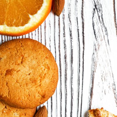 Portakallı bisküviler beyaz ahşap zemin üzerinde portakal dilimleri ve bademlerle yatar. Yakın plan.