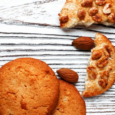 Portakallı bisküviler beyaz ahşap zemin üzerinde portakal dilimleri ve bademlerle yatar. Yakın plan.