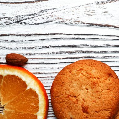 Portakallı bisküviler beyaz ahşap zemin üzerinde portakal dilimleri ve bademlerle yatar. Yakın plan.