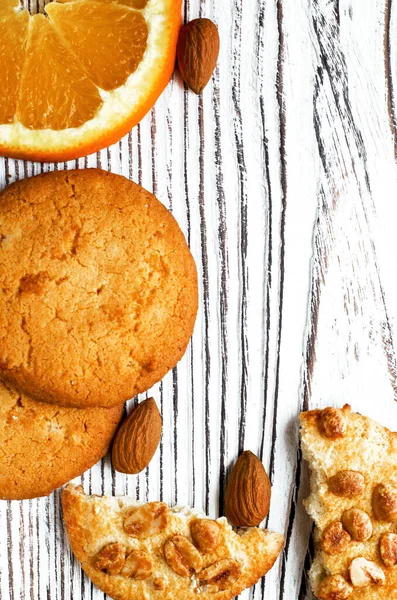 Orange biscuits lie on a white wood background with orange wedge and almonds. Close-up — Stock Photo, Image