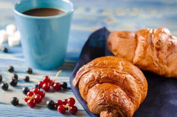 French breakfast: Ruddy croissants with forest berries and a cup of coffee with milk stand on a table
