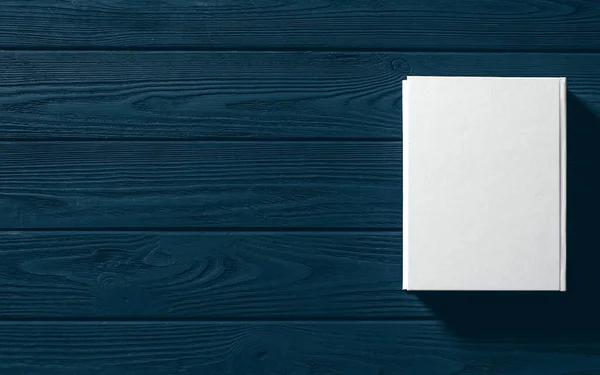 Beyaz kaplı kitap ahşap bir masanın üzerinde..