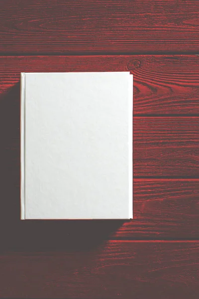 O livro de capa branca está em uma mesa de madeira texturizada . — Fotografia de Stock