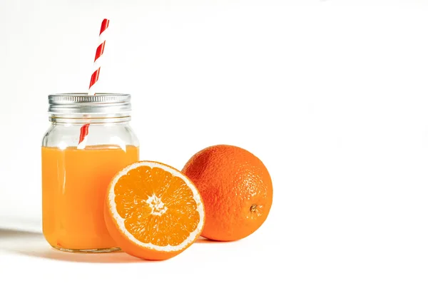 Frasco de vidro com um tubo com suco de laranja recentemente espremido fica em um fundo branco ao lado de laranjas frescas — Fotografia de Stock