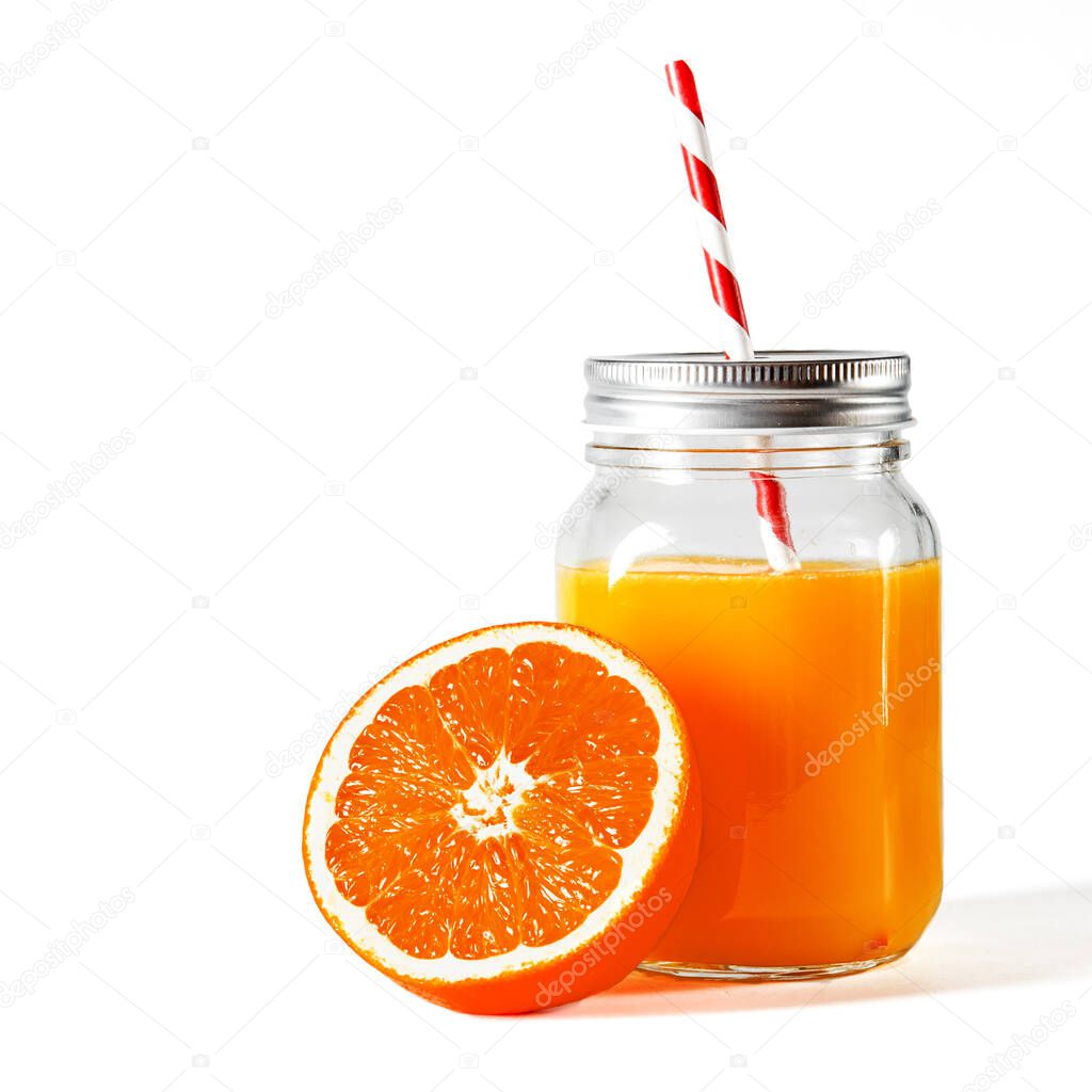 Glass jar with a tube with freshly squeezed orange juice stands on a white background next to fresh oranges