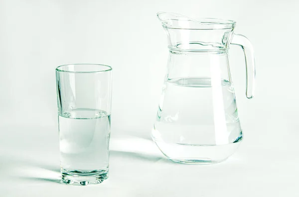Pure clear water in a glass glass and glass jug stands on a white background