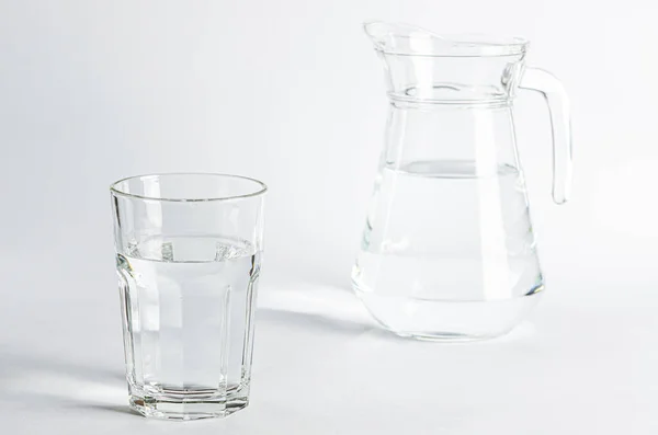Cam bardakta saf temiz su ve cam sürahi beyaz arka planda duruyor.