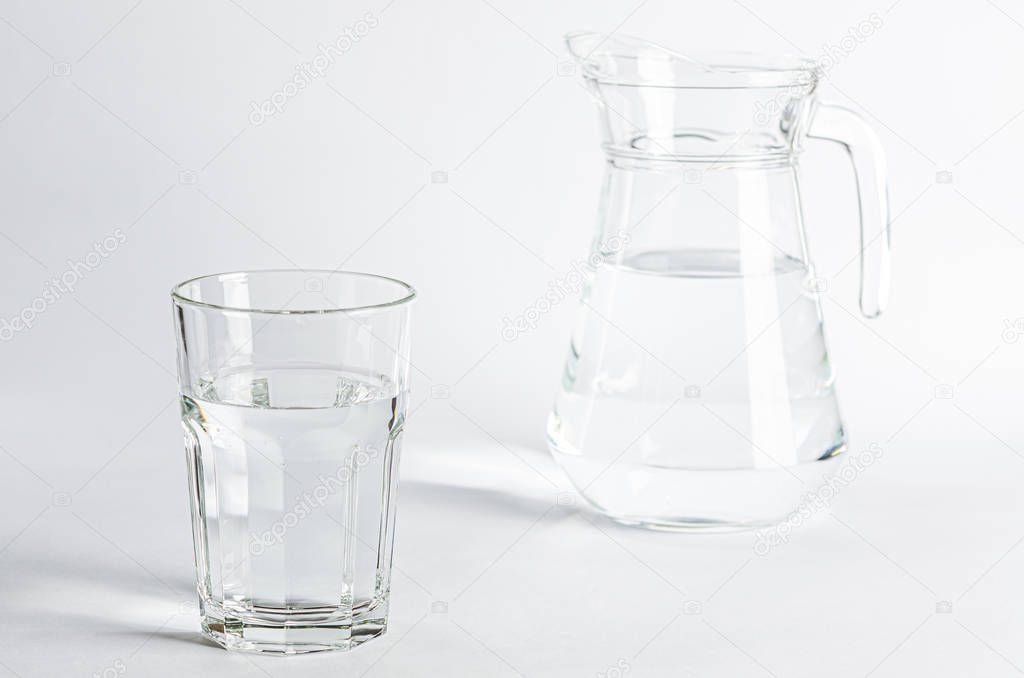 Pure clear water in a glass glass and glass jug stands on a white background