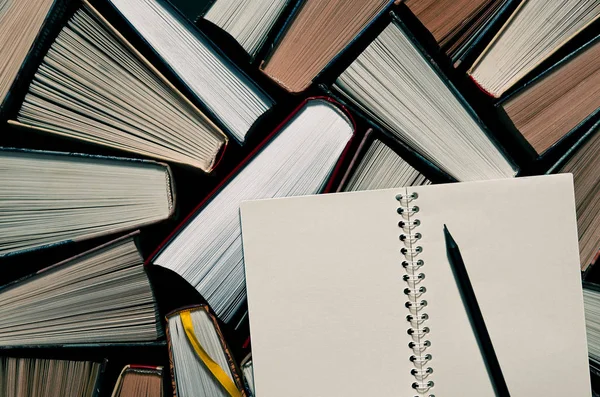 Sebuah pensil hitam dengan sebuah buku catatan terletak pada buku-buku terbuka warna-warni di perpustakaan — Stok Foto