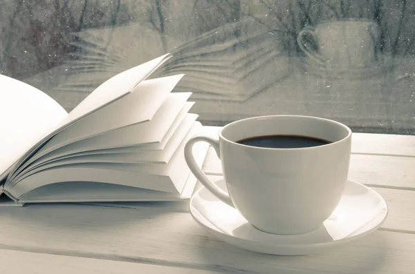 Samimi ev hayatı: beyaz kahve fincanı ve beyaz kitap dışarıdaki kar manzarasına karşı pencere kenarında açıldı.