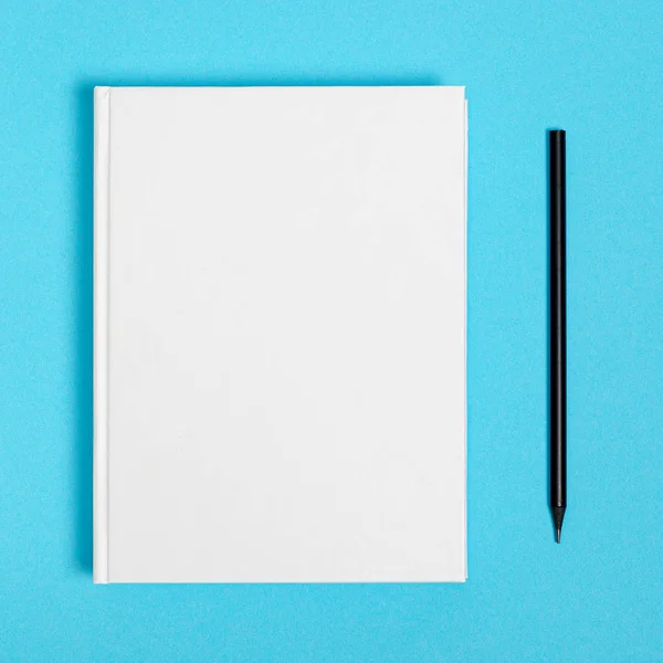 Mockup of closed blank square book and black pencil at colored textured paper background — Stok fotoğraf