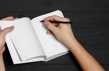 Men's hands hold a white notebook with clean pages and a black pencil