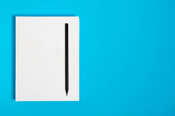 Mockup of closed blank square book and black pencil at colored textured paper background — 스톡 사진