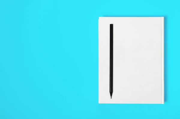 Mockup of closed blank square book and black pencil at colored textured paper background — Stok fotoğraf