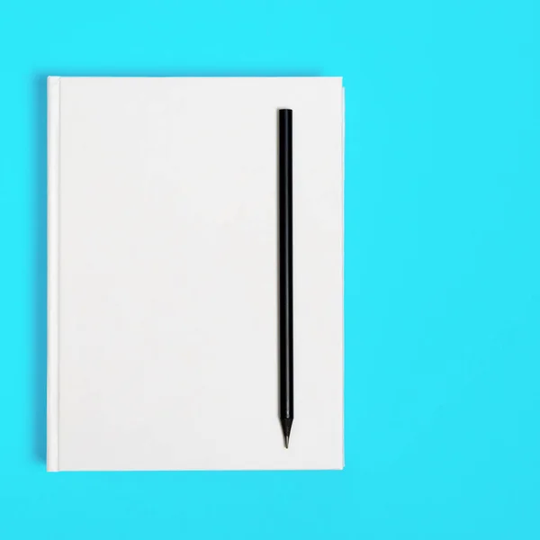 Mockup of closed blank square book and black pencil at colored textured paper background — Stockfoto