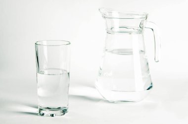 Bardaktaki saf temiz su ve sürahi beyaz arka planda duruyor.