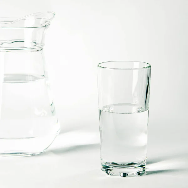 ガラスの中の清らかな水と白い背景の上に立つジャグ — ストック写真