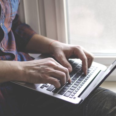 Ev ofisinde dizüstü bilgisayar kullanan adam. Klavyede yazan erkek eller