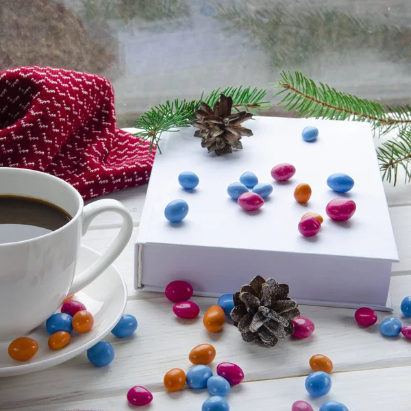 The white book lies on a white wooden window sill next to chocolates and spruce branch — Stock Photo, Image