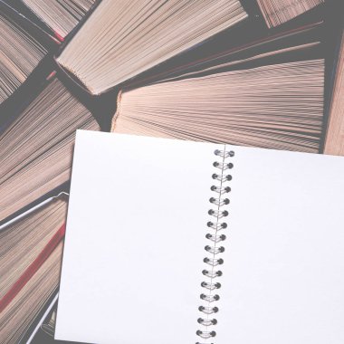 Temiz sayfaları olan beyaz bir defter eski renkli kitapların üzerinde duruyor.