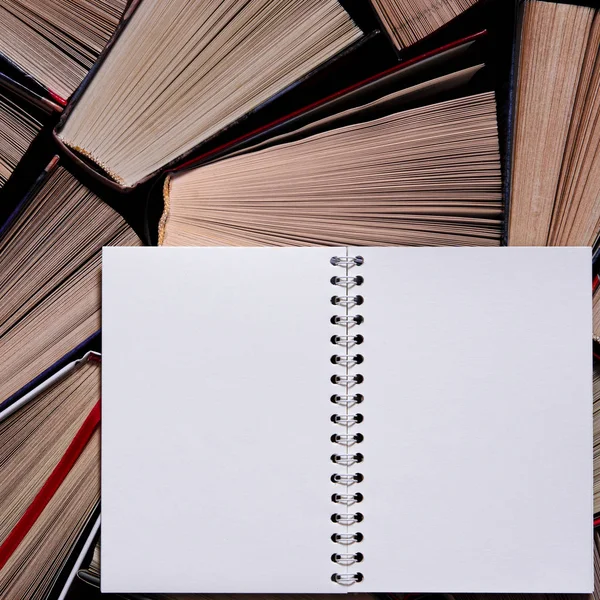 Белая тетрадь с чистыми страницами опирается на старые разноцветные книги — стоковое фото