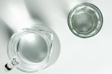 Cam bardakta saf temiz su ve cam sürahi beyaz arka planda duruyor.