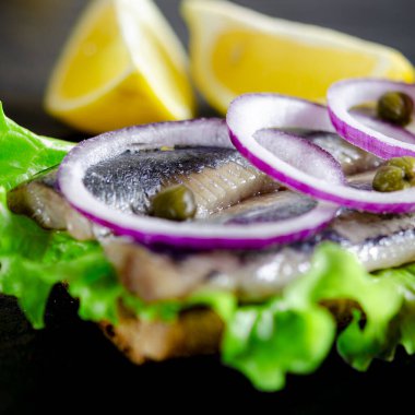 Appetizing smorrebrod with Norwegian herring, lettuce, blue onion, lemon and tomato lies on a wooden board