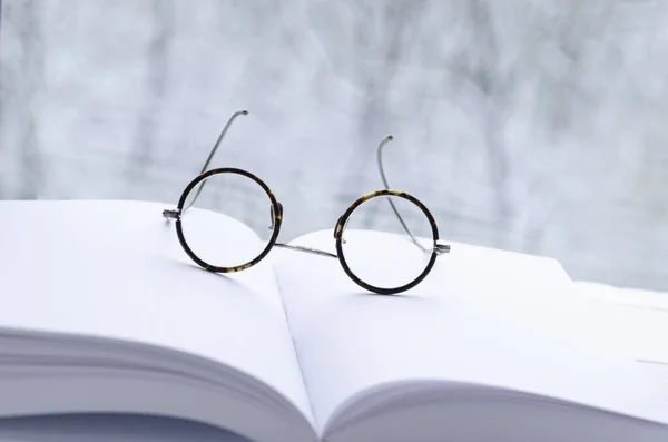 Round vintage reading glasses lie on a white notebook with clean pages
