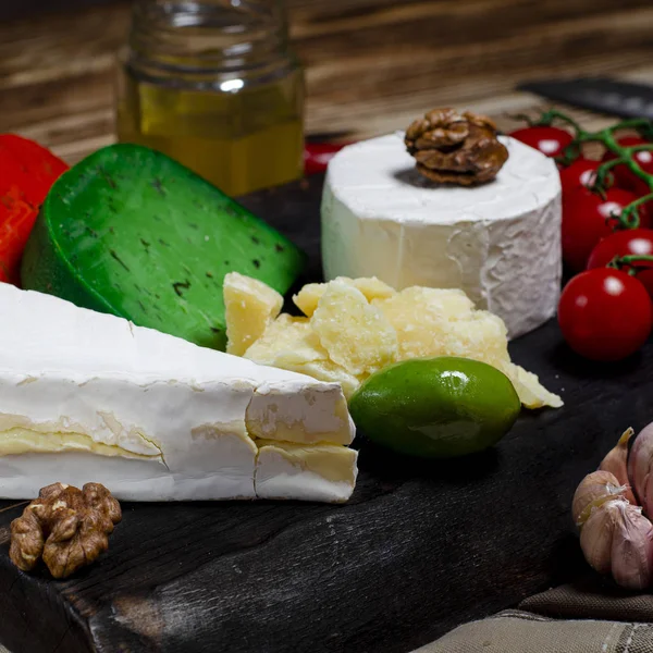 Set de quesos con diferentes quesos, aceitunas, chile, baguette y carne se encuentra en una tabla de madera —  Fotos de Stock