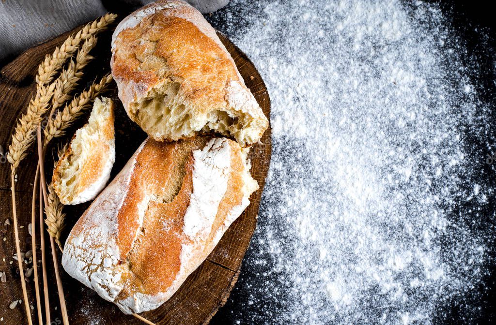 Fresh crispy homemade bread made of white flour lies on a round board next to flour