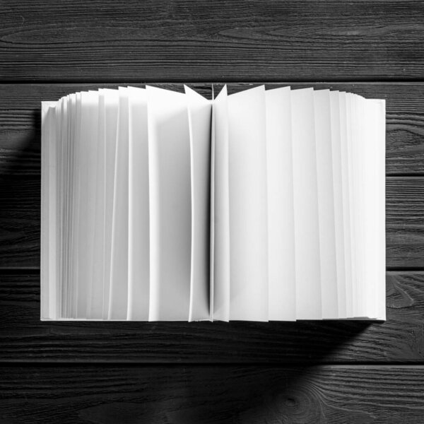 A white book with white pages lies on a black wooden background. Close-up