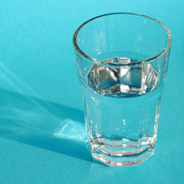 Temiz, berrak suyu olan bir bardak yeşil gölgeli mavi bir zeminde duruyor.