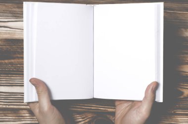 Erkeklerin elleri, arka planda boş kapağı olan açık bir kitabı tutuyor. Boş kare kitapların maketi