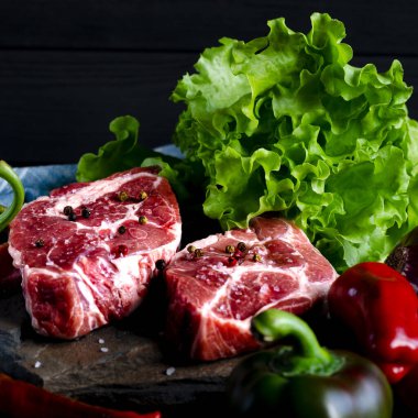 Et konsepti. Et biftekleri masada sebzelerle pişirmeye hazır. Yakın plan.