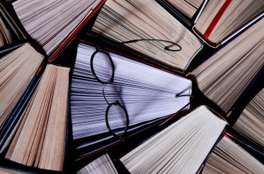 Birçok açık renkli kitap rafta eski yuvarlak bardakların yanında duruyor.