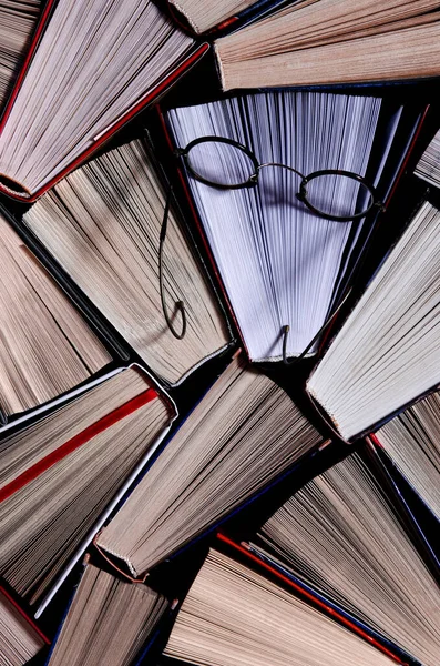 Birçok açık renkli kitap rafta eski yuvarlak bardakların yanında duruyor.