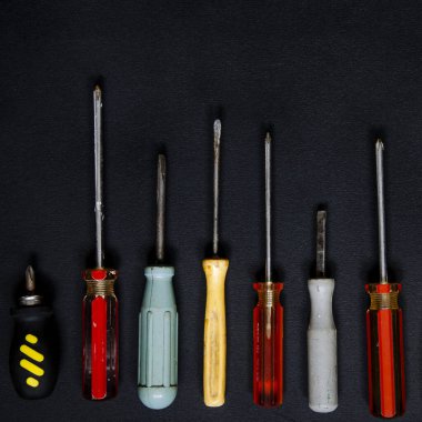 Onarım ve iş için farklı şekillerde, boyutlarda ve renklerde tornavidalar siyah bir arkaplanda yatar