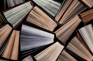 Kitaplar. Birçok renkli, kalın, karanlık arka planda duran kitap var. Okumaya hazır