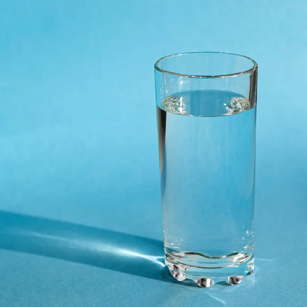 A glass with clean clear clear water stands on a blue background with green shadows