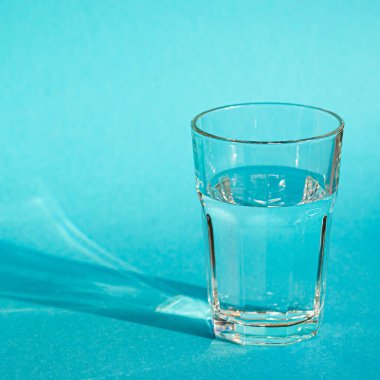 Temiz, berrak suyu olan bir bardak yeşil gölgeli mavi bir zeminde duruyor.