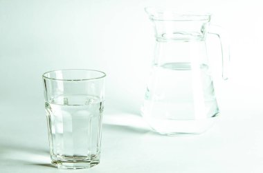 Bardaktaki saf temiz su ve sürahi beyaz arka planda duruyor. izole