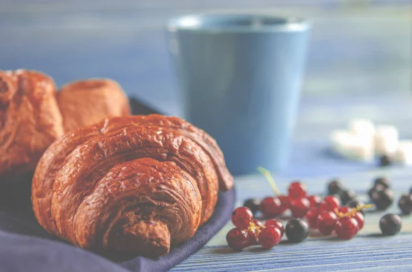 Traditional French breakfast. Croissants with forest berries and a cup of coffee stands on a wooden table. Close-up