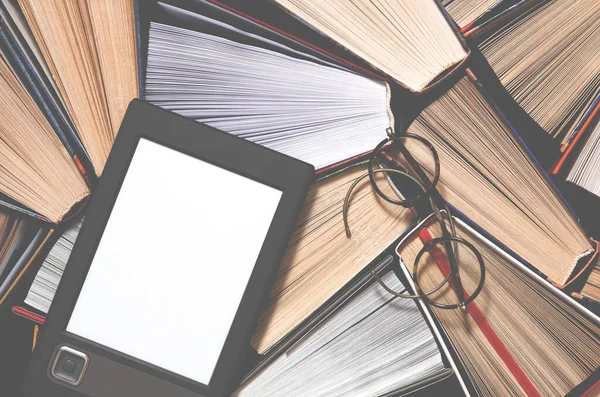 The e-book with a white screen lies on the open multi-colored books that lie on a dark background, ready to read. close-up