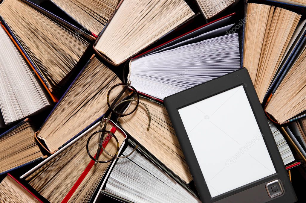 The e-book with a white screen lies on the open multi-colored books that lie on a dark background, ready to read. close-up