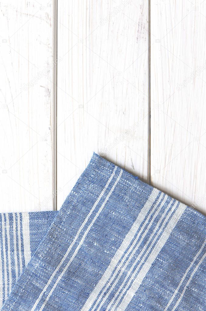 A blue napkin in a white stripe rests on a white wooden table. Close-up