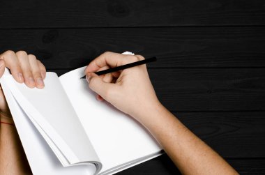 Sapan gibi arka planda bir adamın elinde beyaz bir defter ve siyah bir kalem. Yakın plan.